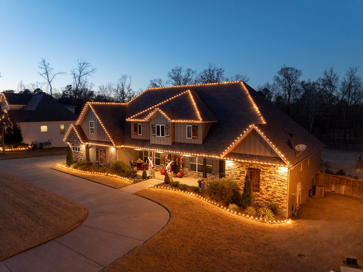 A full holiday roofline display lit at dusk on a stone and shake home