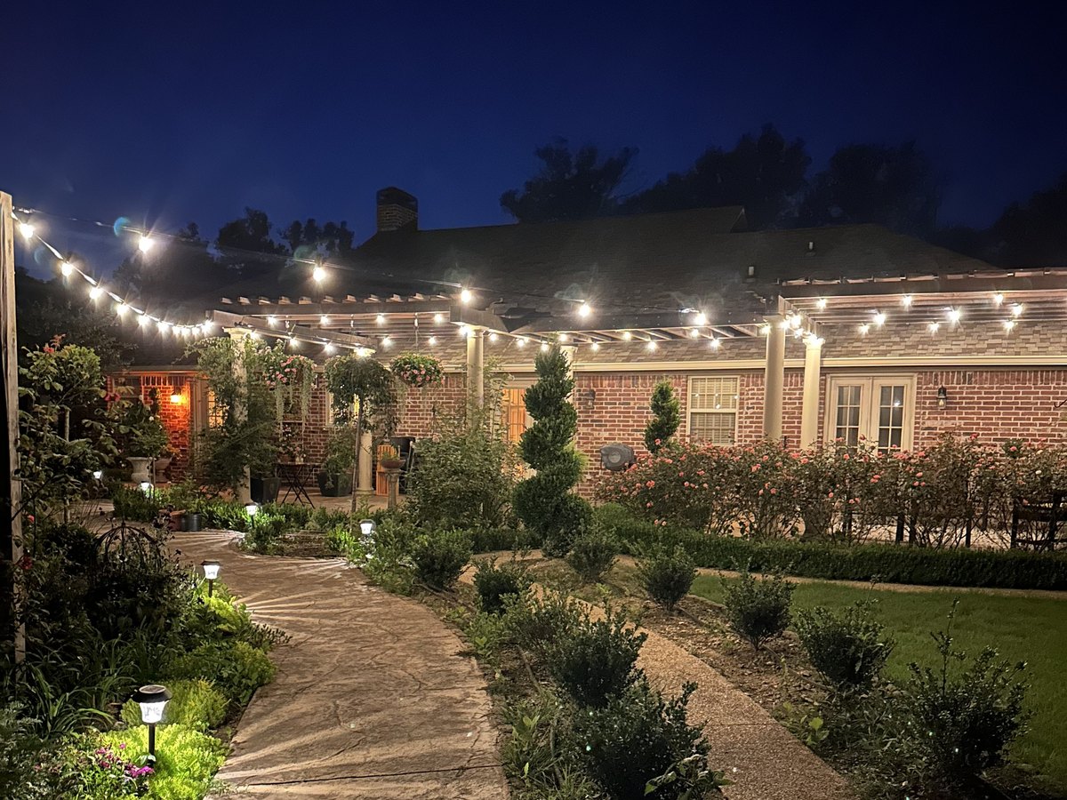 A lit garden path and string lighting across a pergola at night